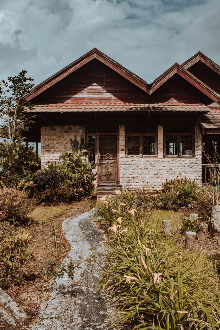 who-we-are Quaint rustic house with garden pathway in Cianjur, West Java, showcasing traditional architecture and lush greenery.