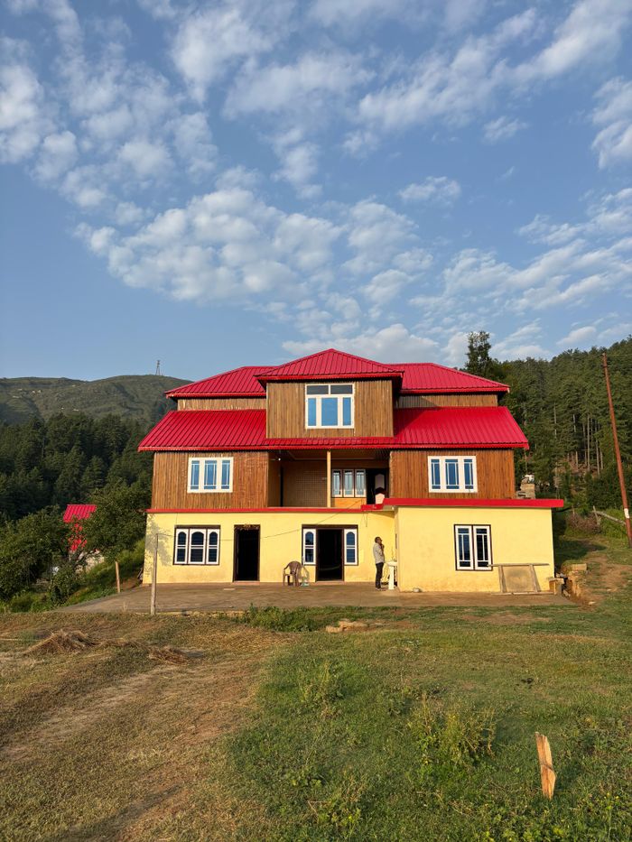 service-01 A picturesque wooden house with a vibrant red roof in a lush green countryside setting.