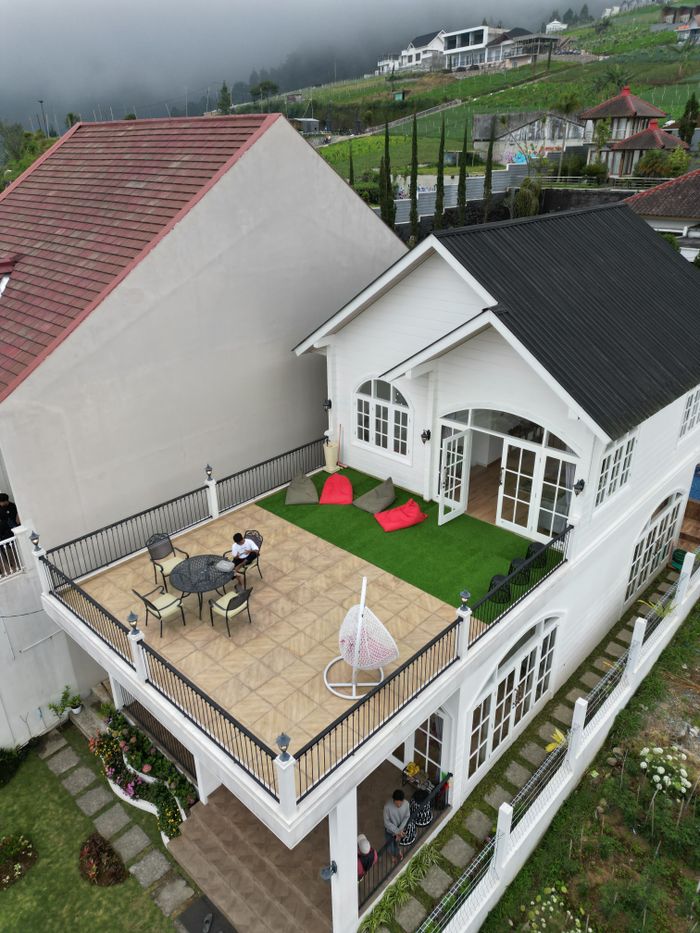 service-05 Aerial view of a modern house with a rooftop terrace in a scenic, lush green area.
