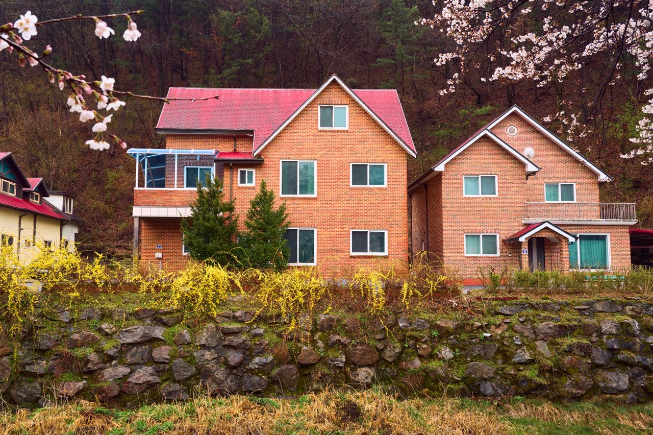 service-06 Brick houses with red roofs surrounded by spring blossoms, showcasing idyllic countryside living.